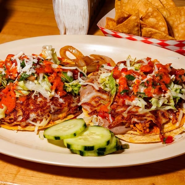 Loaded Mexican-style plate with sauced enchiladas, shredded lettuce, onions, salsa, cucumber slices, tortilla chips, and dipping sauce.